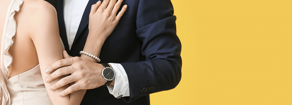 closeup of a man and woman embracing wearing formal clothes. Woman has a pearl bracelet and man is wearing an analog watch